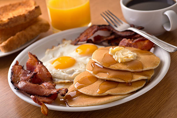 A delicous home style breakfast with crispy bacon, eggs, pancakes, toast, coffee, and orange juice.